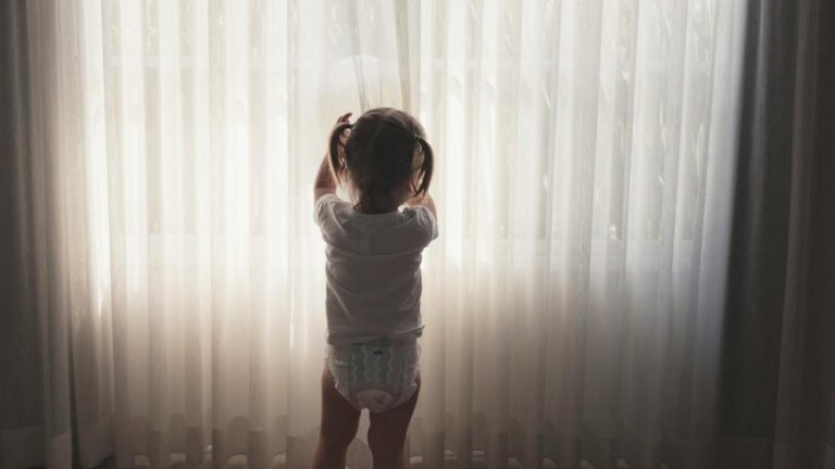Kleinkind steht selbstständig am Fenster – Entwicklung hin zu mehr Selbstständigkeit