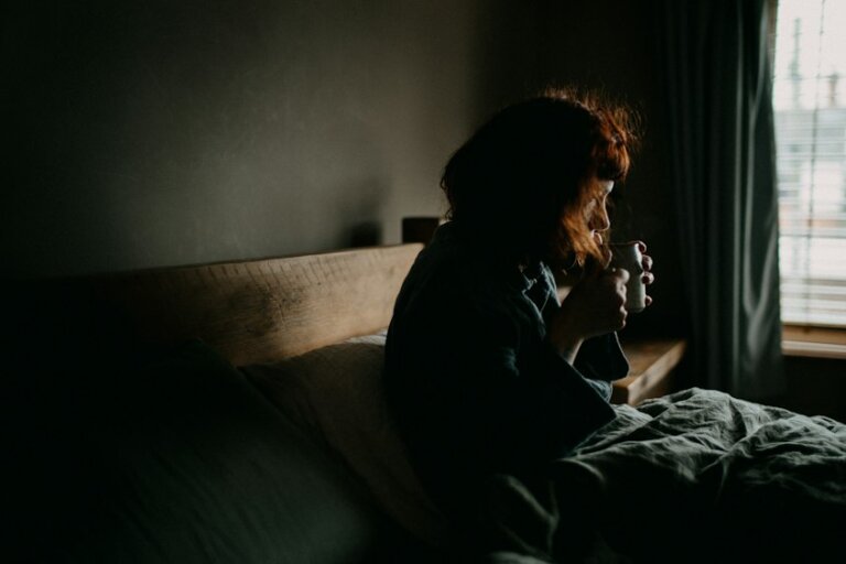 Frau mit Tasse im Schlafzimmer als Symbol für wechselnde Tageszeiten und Schichtarbeit